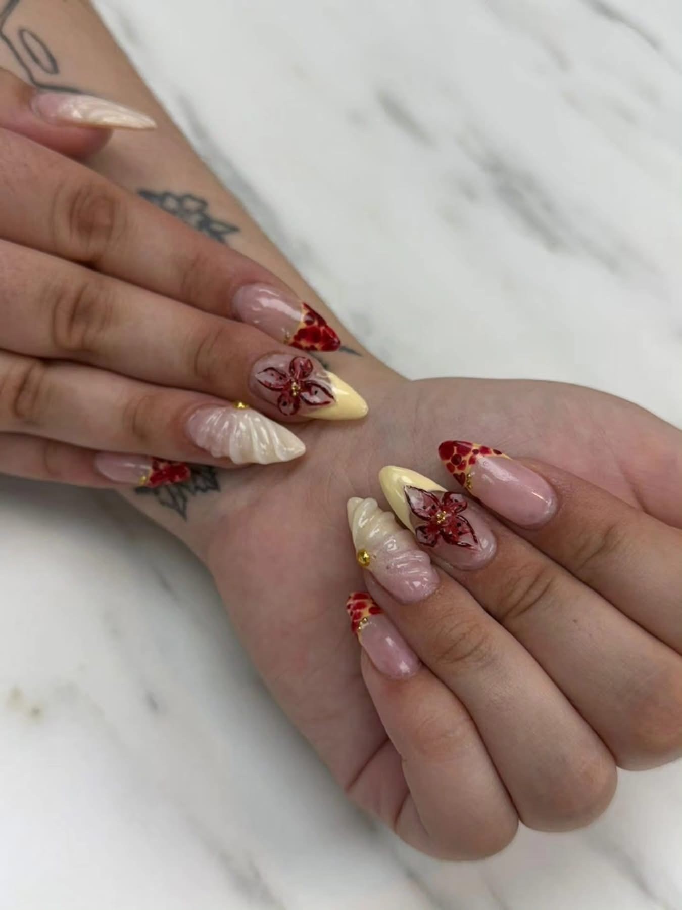 Cream and red stiletto nails with 3D floral art and gold details at Ash's Lashes and Esthetics