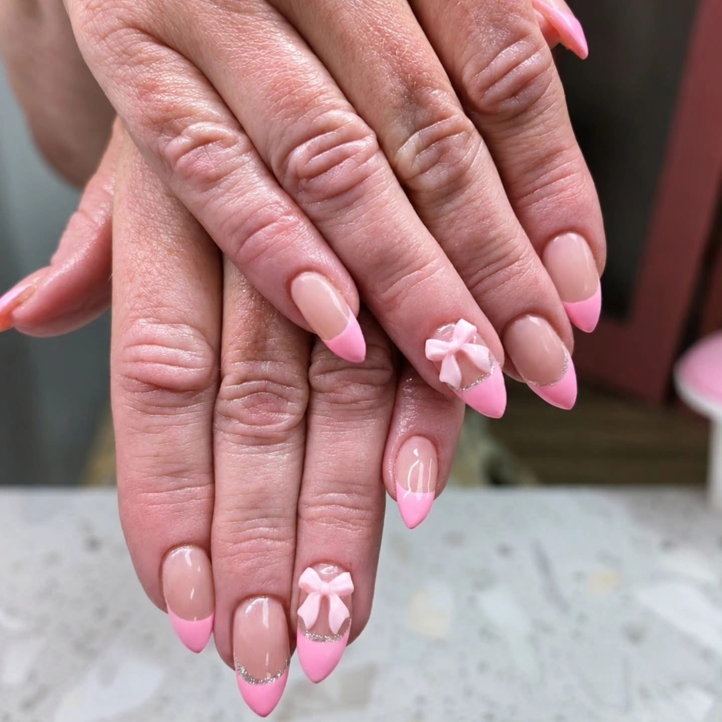 Pink ombre almond nails with 3D bow accent and glitter tips at Ash's Lashes and Esthetics