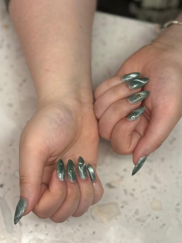 Metallic green stiletto nails with gold star details at Ash's Lashes and Esthetics