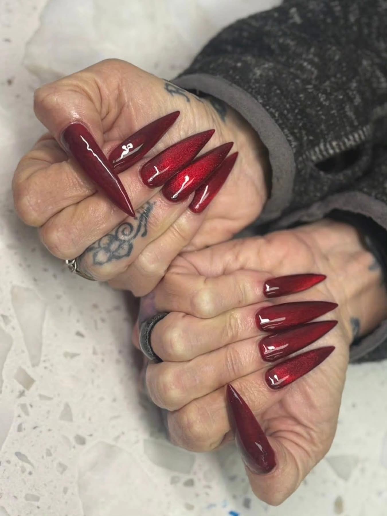 Deep burgundy red stiletto nails with glossy chrome finish at Ash's Lashes and Esthetics