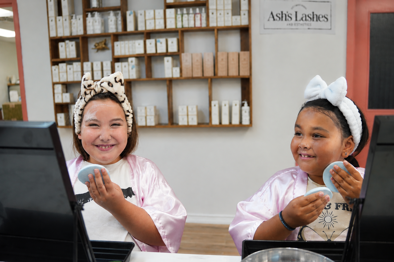 Two girls in pink robes with spa headbands enjoying a birthday party at Ash's Lashes