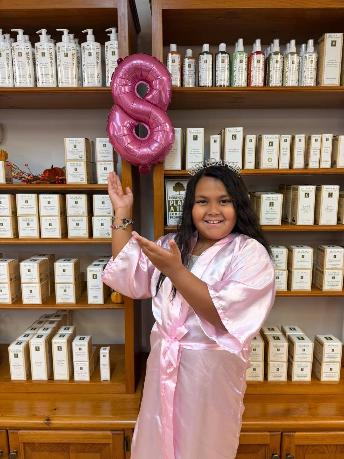 Birthday girl in a pink satin robe holding a pink number 8 balloon and wearing a birthday crown at Ash's Lashes