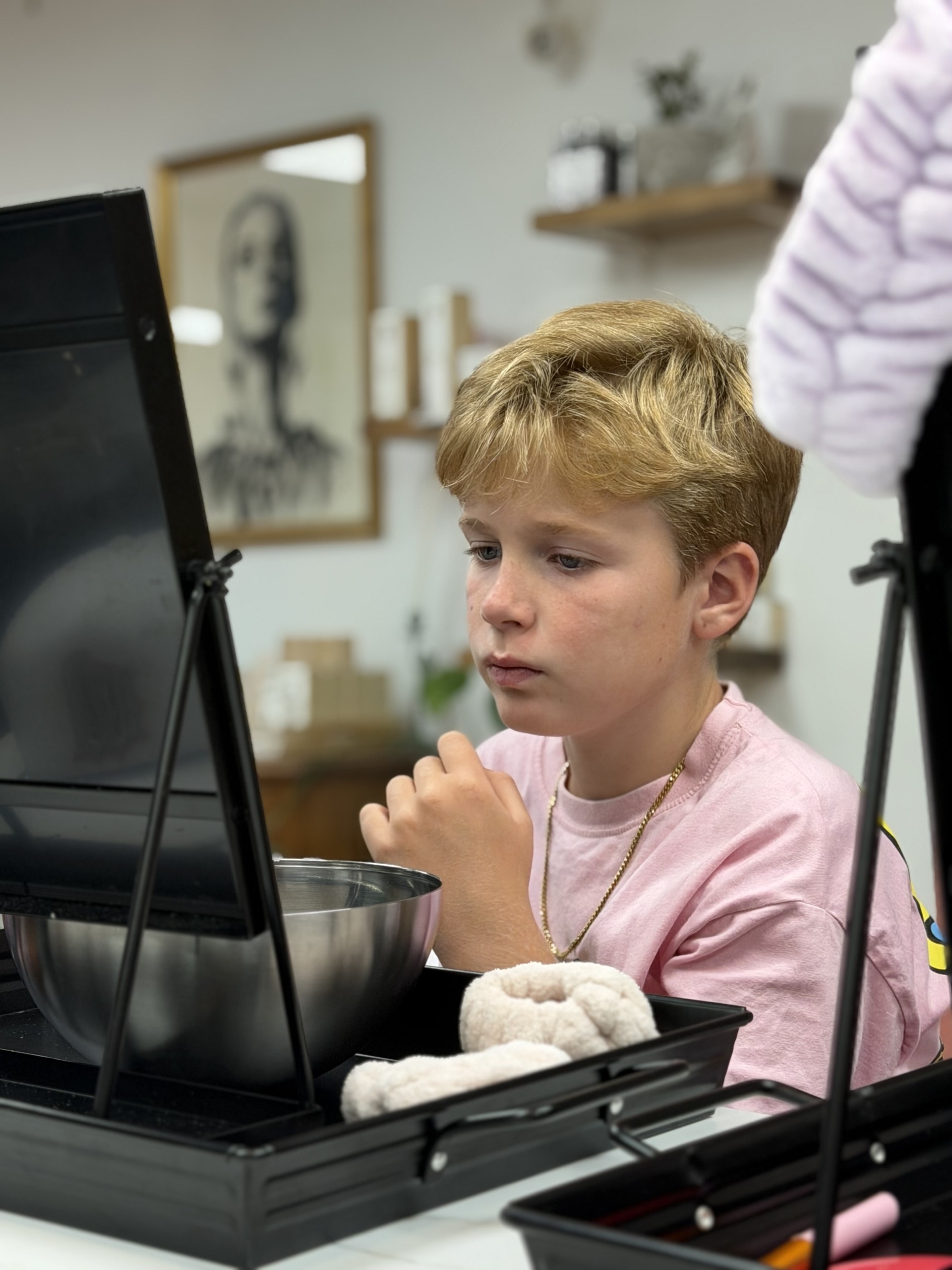 Young boy in a pink shirt concentrating on his skincare treatment at Ash's Lashes birthday party