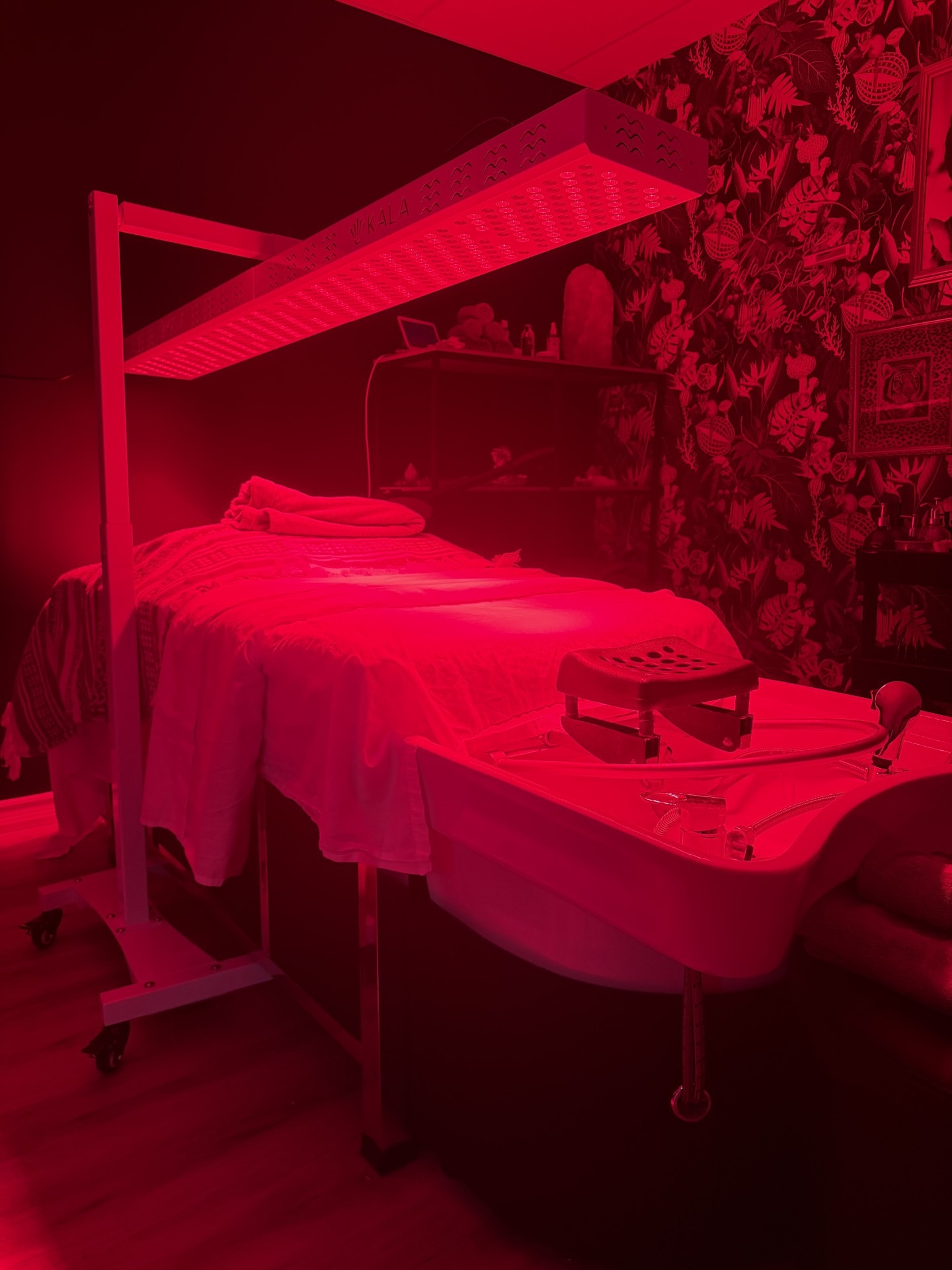 Red light therapy treatment room at Ash's Lashes and Esthetics with glowing red LED panel over a treatment bed