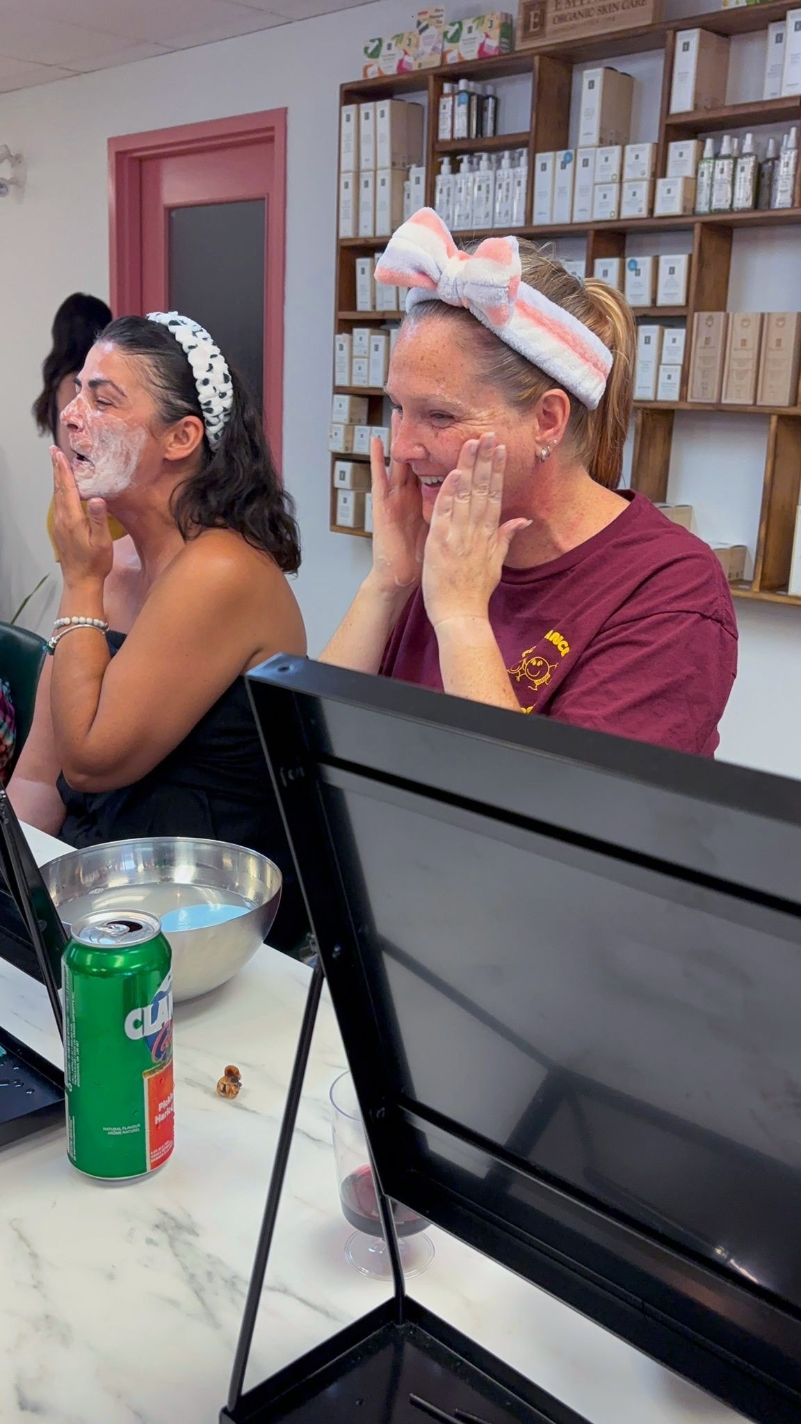 Two women laughing while applying face masks during a You Dew You skincare event at Ash's Lashes