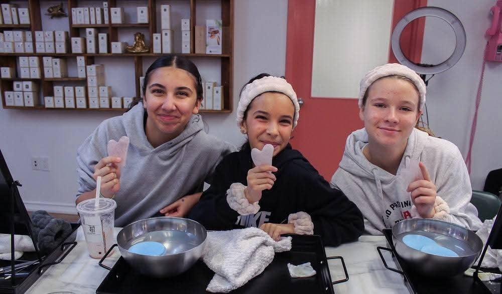 Three girls holding gua sha tools and smiling during a You Dew You guided facial event at Ash's Lashes
