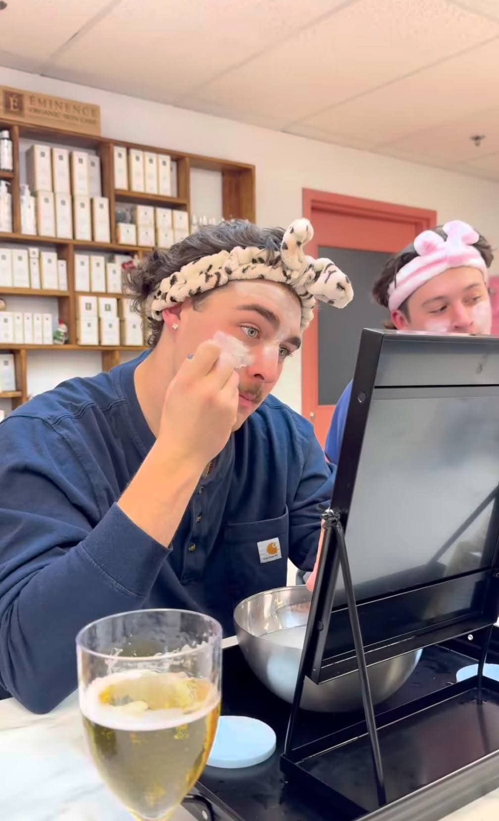 Two young men in spa headbands applying skincare products and laughing during a You Dew You event at Ash's Lashes